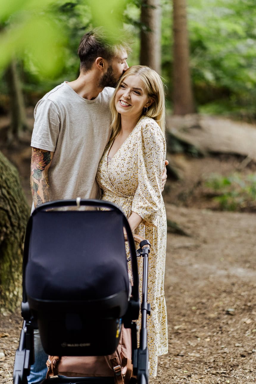 Ein glückliches Paar spaziert im Wald mit ihrem Baby im Kinderwagen, umgeben von grünen Bäumen und frischer Luft.