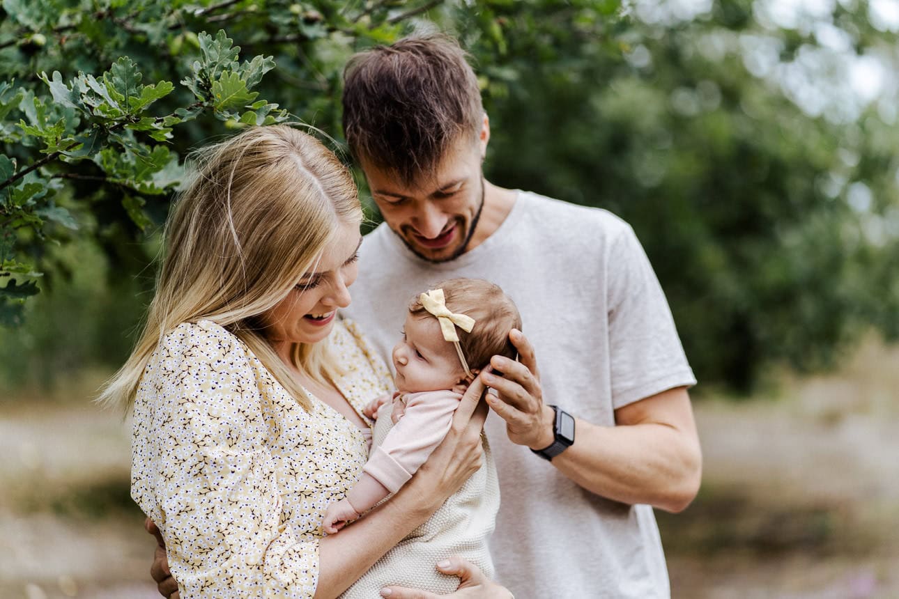 Eine Familie mit ihrem Baby unter einem Baum, fotografiert von einem Familien-Fotografen in Münster.