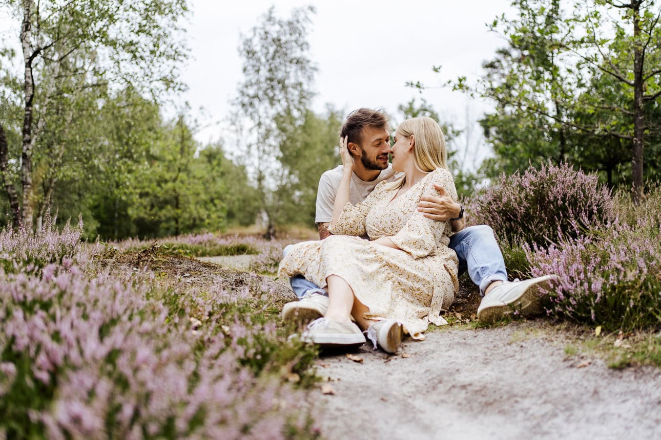 Mann und Frau sitzen auf einem schmalen Pfad in der Heide, umgeben von Heidekraut und der friedlichen Natur.