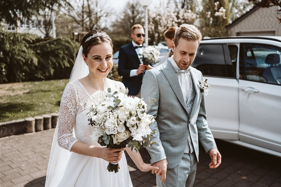 Ein Hochzeitspaar geht Hand in Hand zur Trauung, strahlend und glücklich.