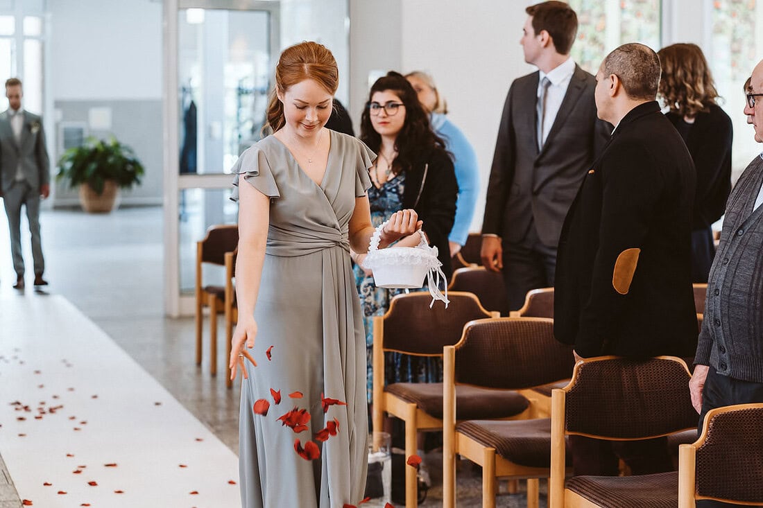 Die Trauzeugin in einem eleganten grauen Kleid schreitet den Gang entlang, während die Gäste gespannt zuschauen.