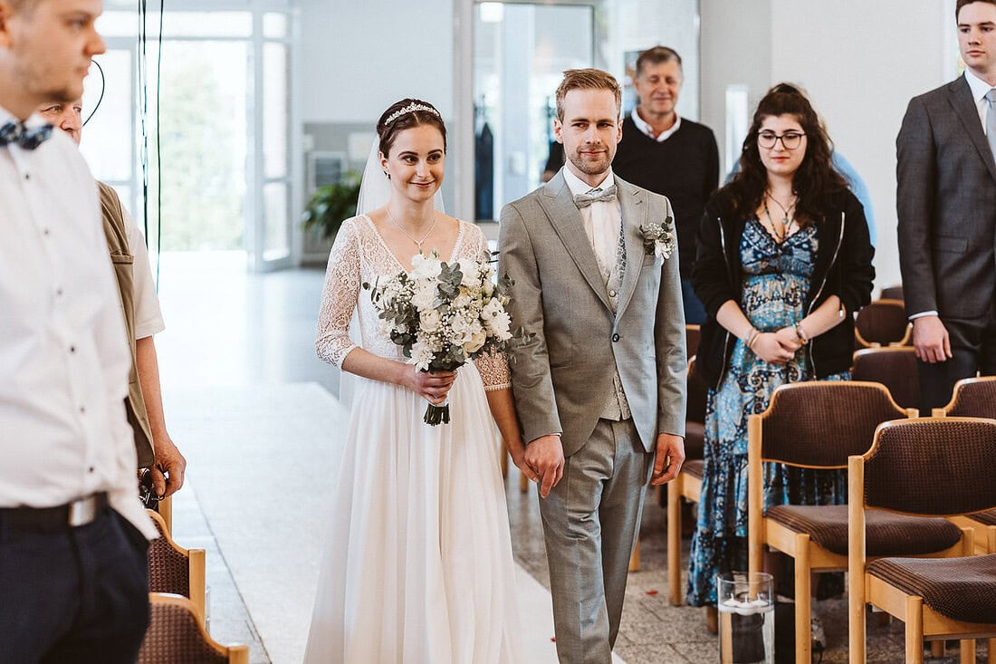 Ein Brautpaar geht glücklich den Gang entlang, umgeben strahlenden Gästen an ihrem Hochzeitstag.