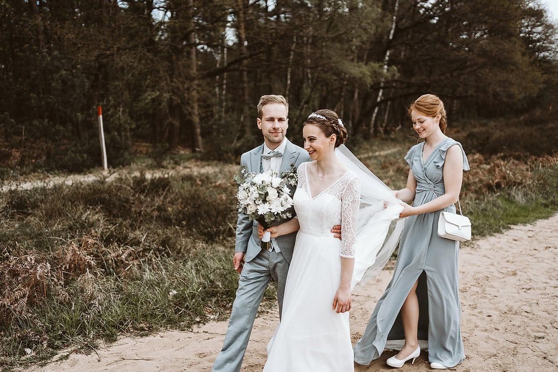 Hochzeitspaar steht mit Trauzeugin auf einem Weg in der Heide.