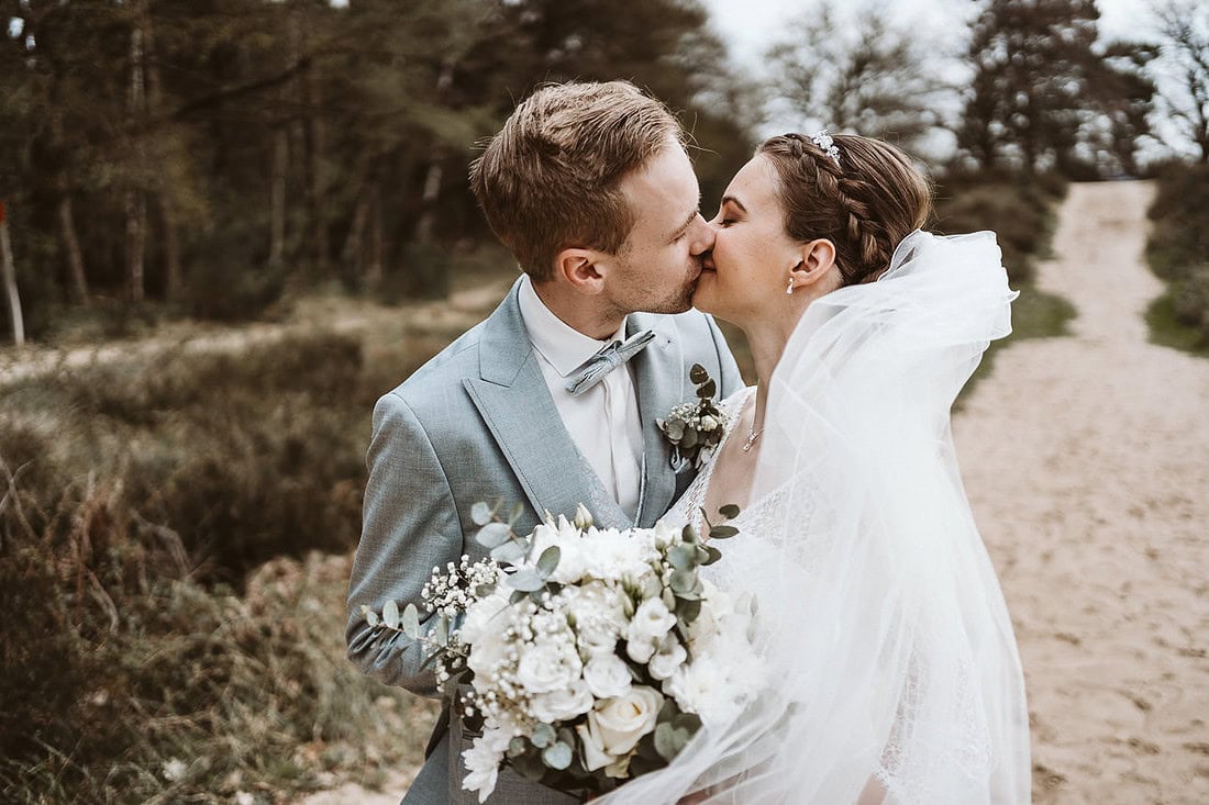 Hochzeitspaar küsst sich in der Heide und ist glücklich.