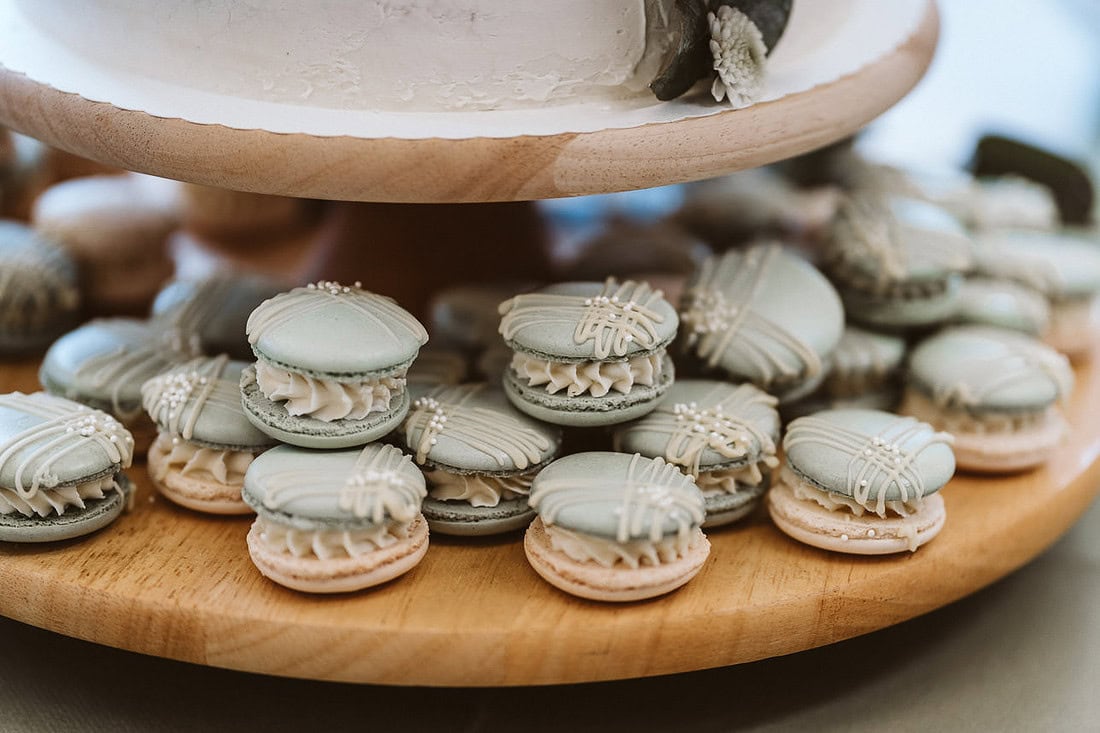 Hochzeitstorte auf einem rustikalen Holzständer, dekoriert mit leckeren Macarons in verschiedenen Farben.