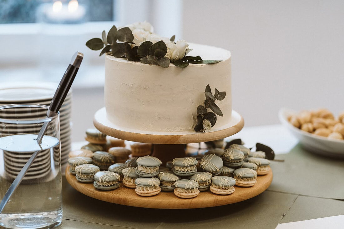 Hochzeitstorte auf einem rustikalen Holzständer, dekoriert mit leckeren Macarons in verschiedenen Farben.