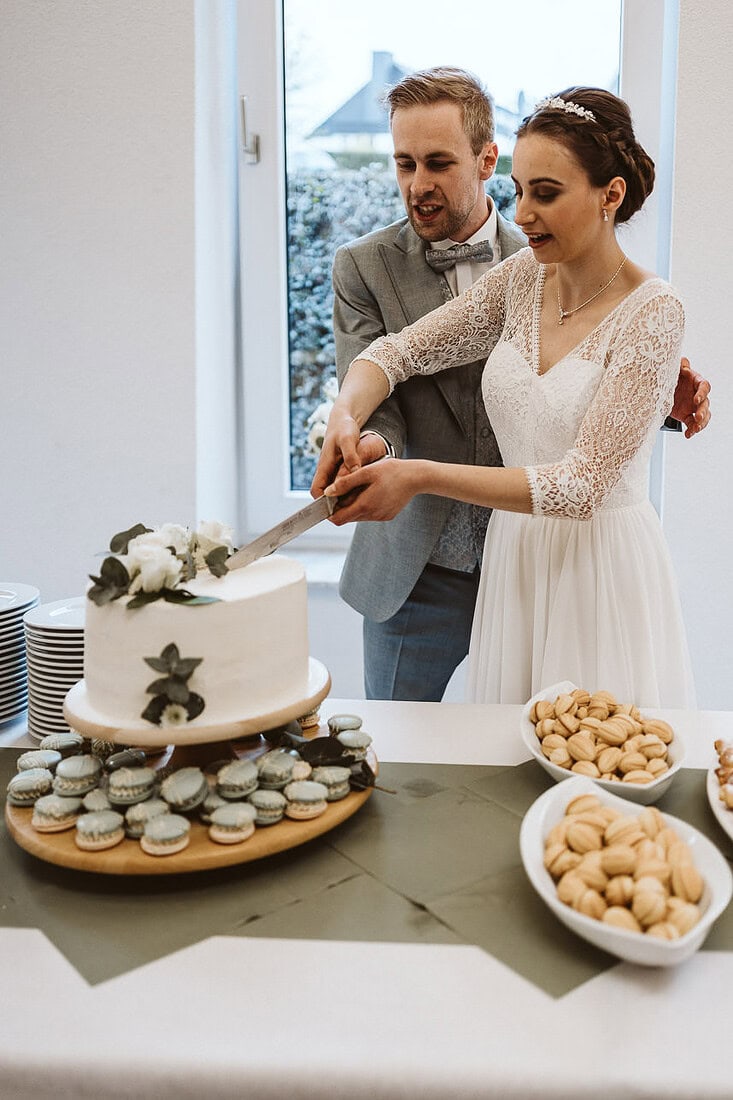 Das Brautpaar schneidet ihre Hochzeitstorte an, umgeben von Freunden und Familie, die diesen besonderen Moment geniessen.