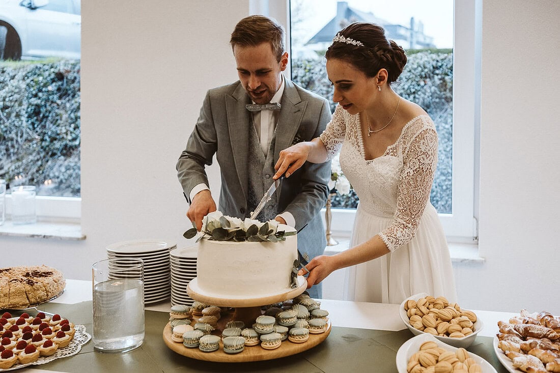 Das Brautpaar schneidet ihre Hochzeitstorte an, umgeben von Freunden und Familie, die diesen besonderen Moment geniessen.