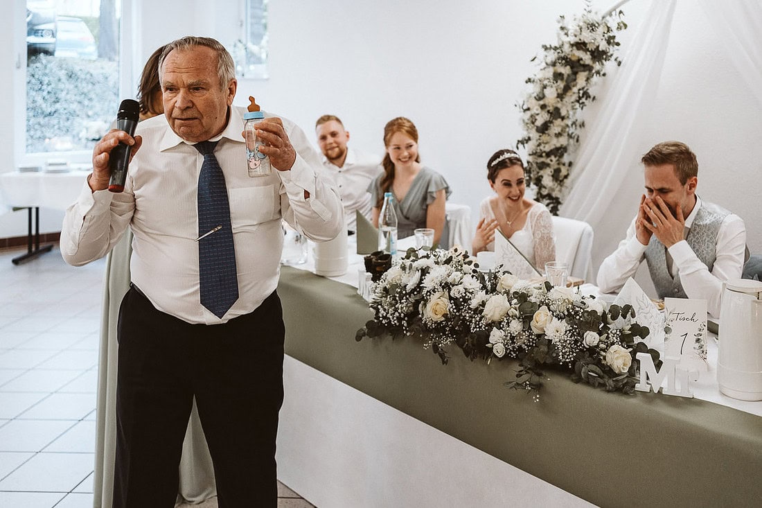 Rede des Brautvater zur Hochzeit. Das glücklich lachende Brautpaar sitzt im Hintergrund.