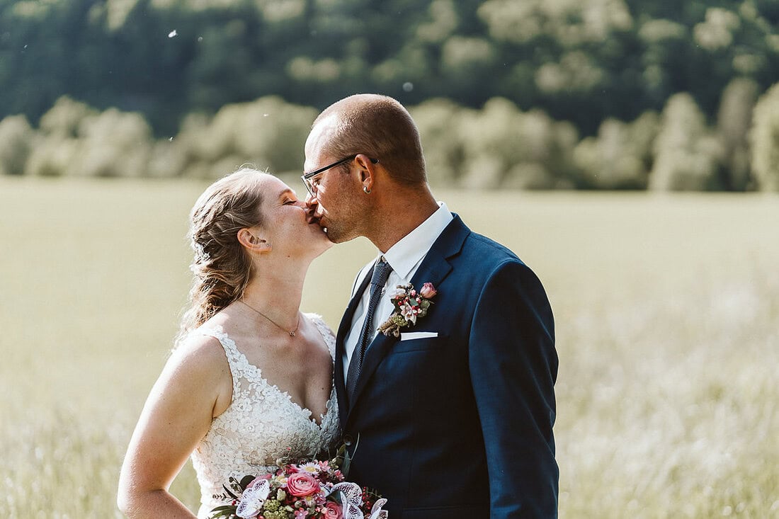 Ein Hochzeitspaar steht auf einer Wiese und küsst sich.