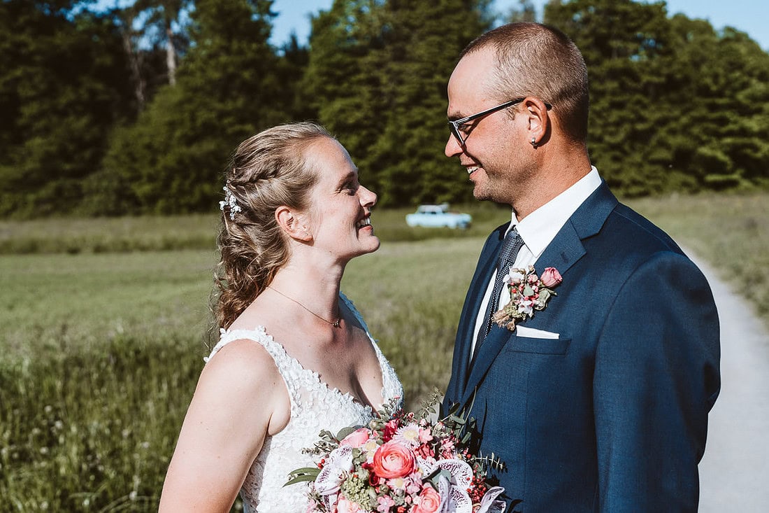 Ein Hochzeitspaar steht auf einem Weg und schaut sich an. Beide lächeln und sind glücklich.