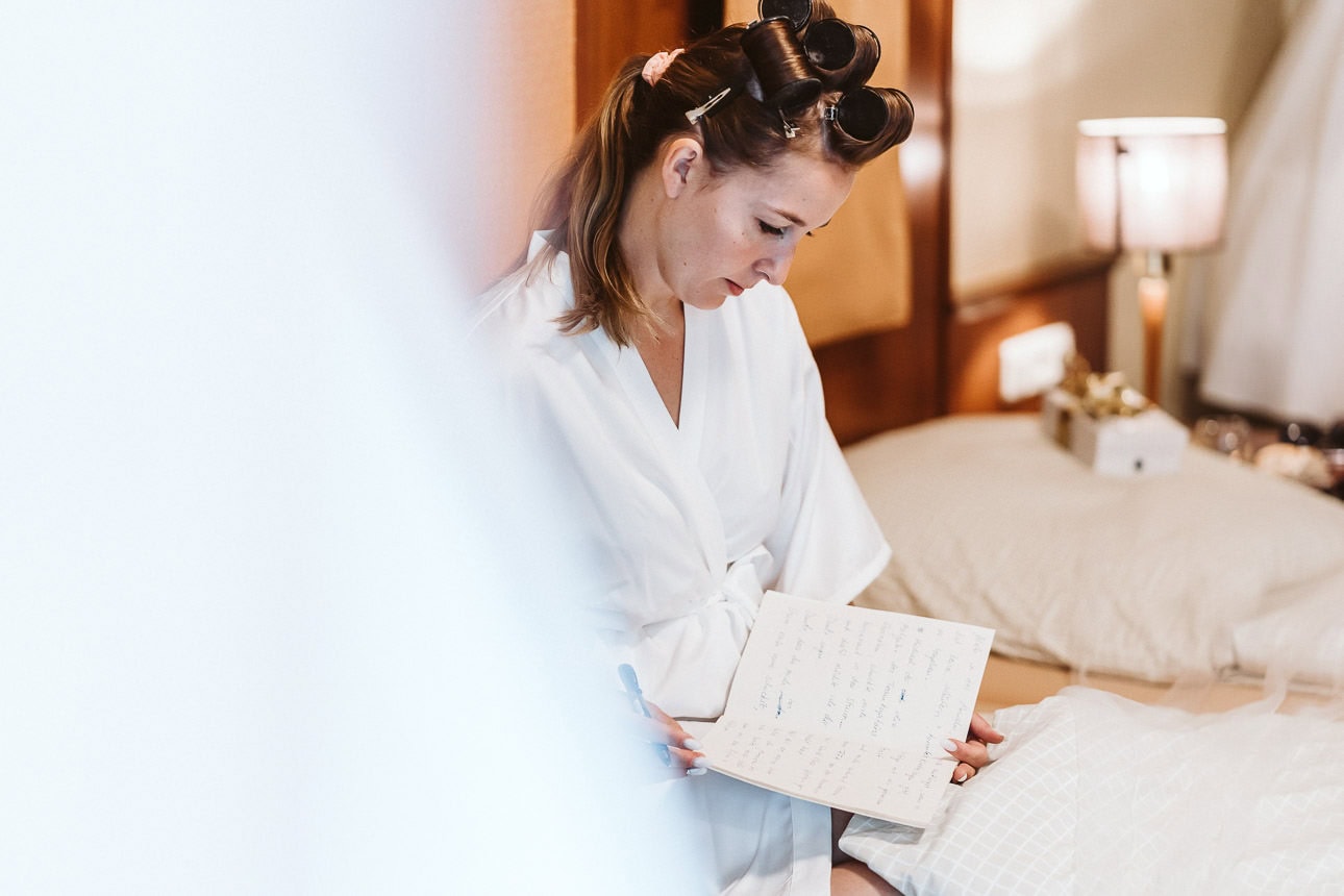 Eine Braut sitzt beim Getting Ready auf dem Bett und macht sich Notizen in ein Buch.