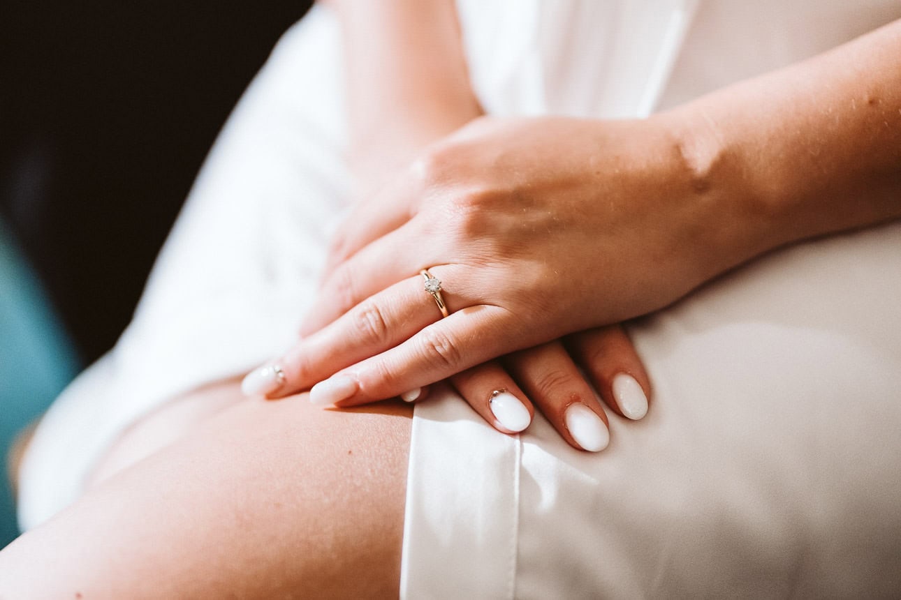 Händer der Braut auf ihrem Oberschenkel. Es ist ein schöner Verlobungsring zu sehen.