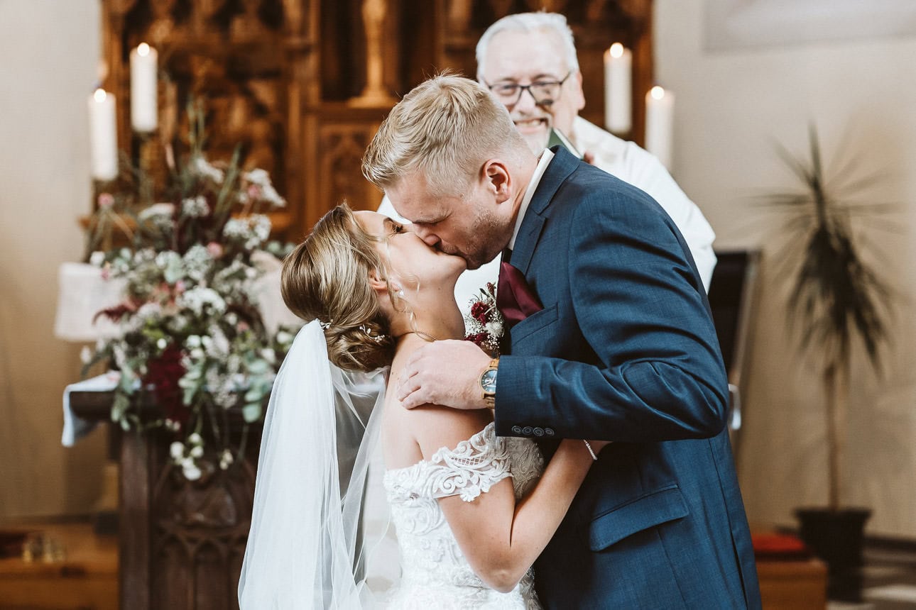 Ein Hochzeitspaar steht vor dem Altar in der Kirche und küsst sich.