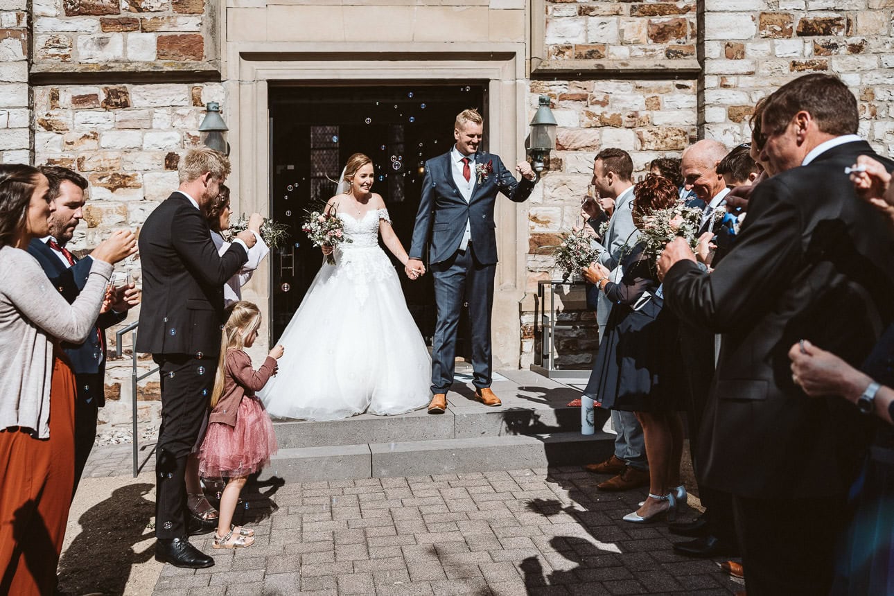 Ein Hochzeitspaar kommt aus der Kirche und wird von den Hochzeitsgästen mit Seifenblasen empfangen.