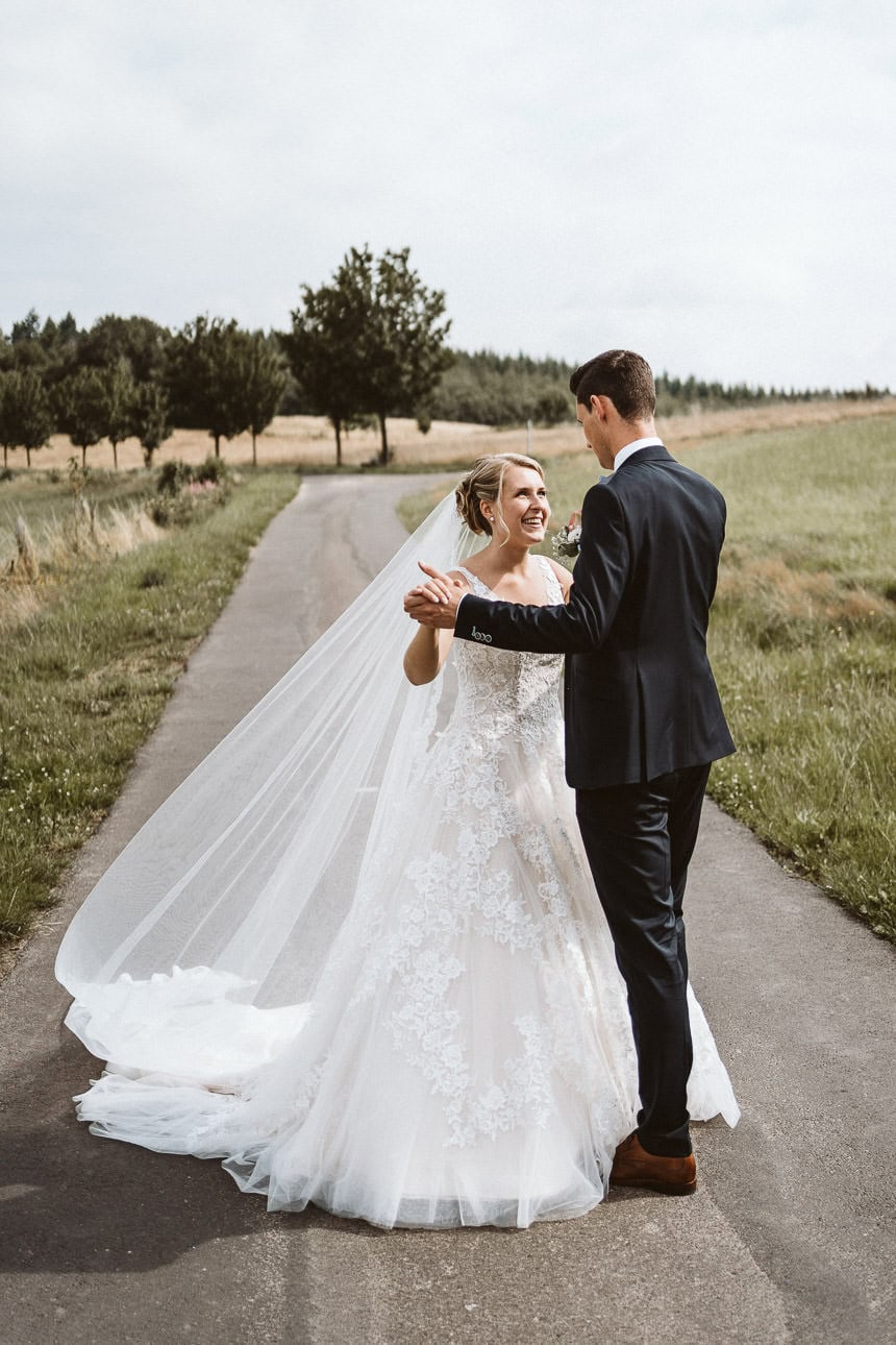 Ein Hochzeitspaar tanzt auf einem Weg und ist glücklich.