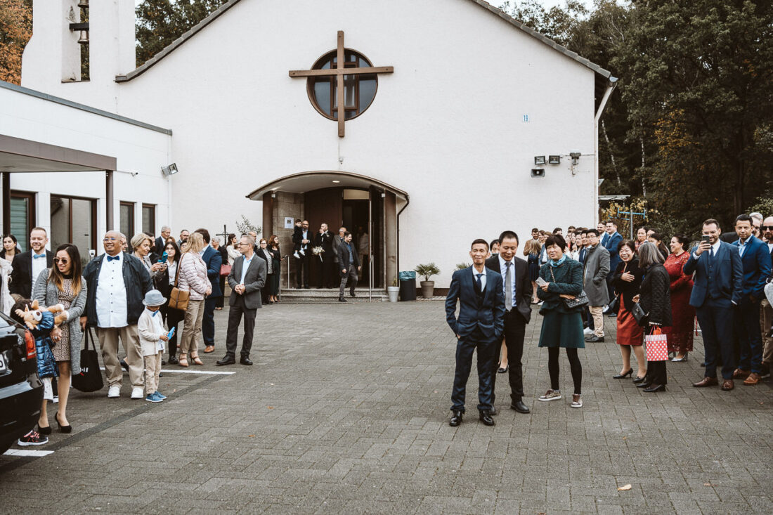 Viele Hochzeitsgäste warten vor einer Kirche.